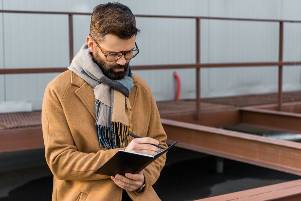 Bearded businessman standing in coat and writing in notebook